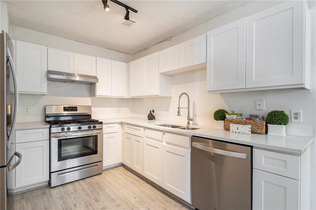 1025 Lakeside Cir, Covington, GA 30016 - kitchen with light countertops, light wood-type flooring, under cabinet range hood, a sink, and appliances with stainless steel finishes