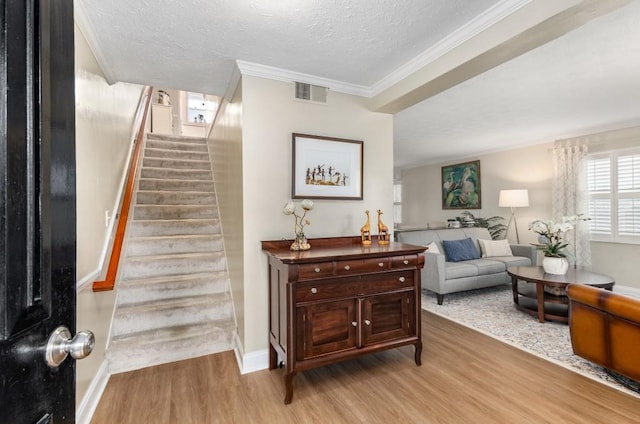 stairs with hardwood / wood-style flooring, ornamental molding, and a textured ceiling