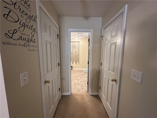 hall with a textured ceiling and light colored carpet