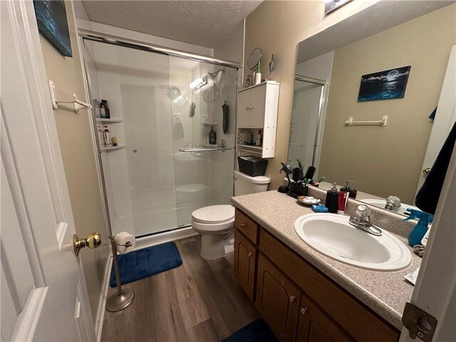 bathroom with an enclosed shower, vanity, a textured ceiling, hardwood / wood-style floors, and toilet