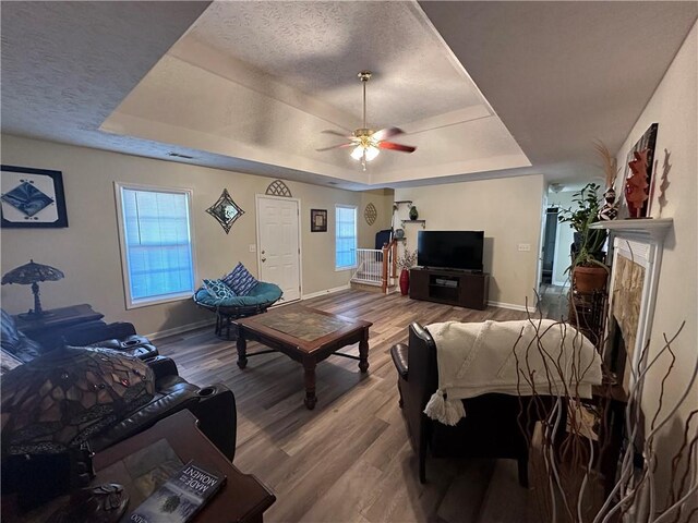 living room with a raised ceiling, ceiling fan, a textured ceiling, and hardwood / wood-style flooring