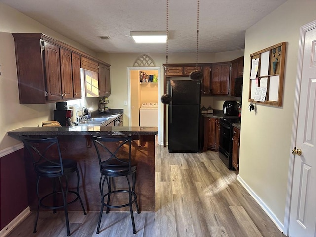 kitchen with sink, light hardwood / wood-style flooring, kitchen peninsula, washer / clothes dryer, and black appliances