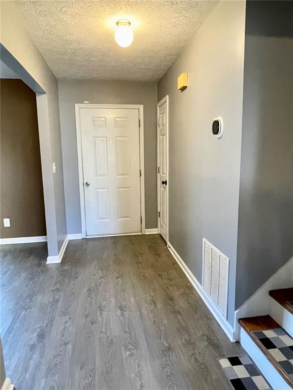 corridor featuring visible vents, a textured ceiling, baseboards, and wood finished floors