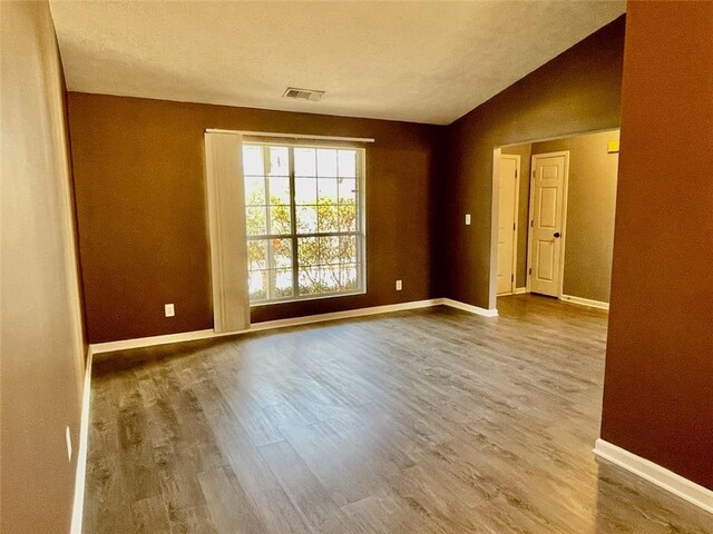 unfurnished room featuring lofted ceiling, wood finished floors, visible vents, and baseboards