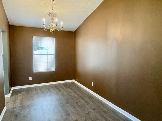 unfurnished room featuring an inviting chandelier, wood finished floors, visible vents, and baseboards