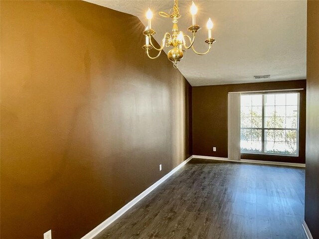 spare room featuring visible vents, baseboards, dark wood-type flooring, and a chandelier