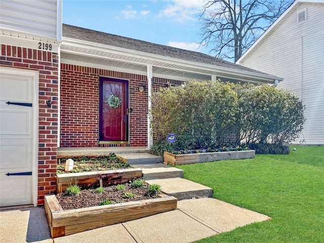 doorway to property featuring a yard, brick siding, and roof with shingles