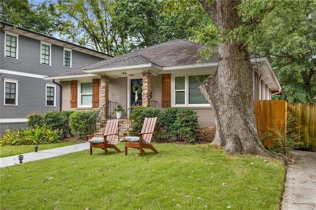 view of front of property featuring brick siding, a shingled roof, a front lawn, and fence