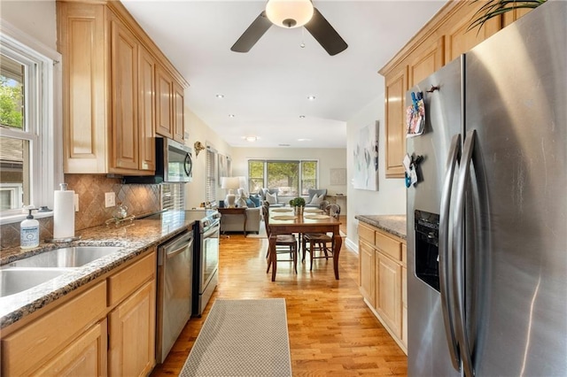 kitchen with light brown cabinets, stainless steel appliances, decorative backsplash, light wood-style floors, and open floor plan