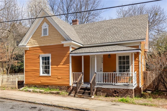 view of front of home featuring roof with shingles, covered porch, a chimney, and fence