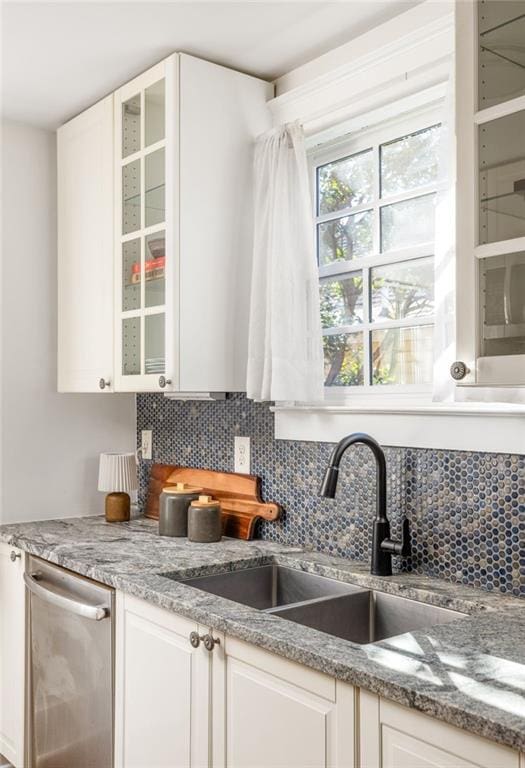 kitchen featuring tasteful backsplash, glass insert cabinets, dishwasher, white cabinets, and a sink