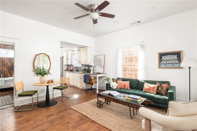 living room featuring a ceiling fan, visible vents, dark wood-style flooring, and baseboards