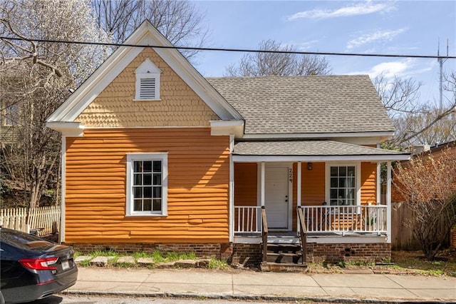 view of front facade with a porch, fence, and roof with shingles