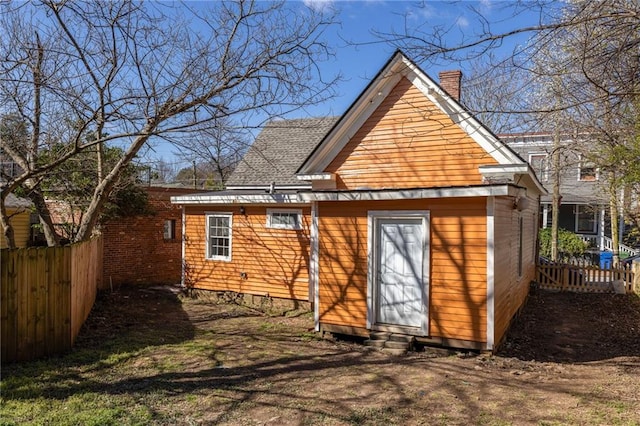 exterior space with a shingled roof, fence, and a chimney