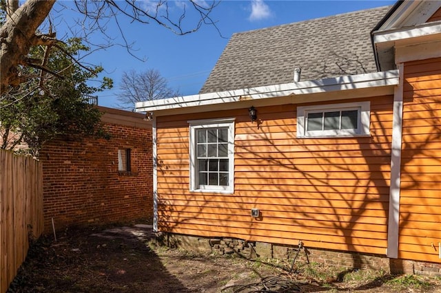 view of property exterior with fence and a shingled roof