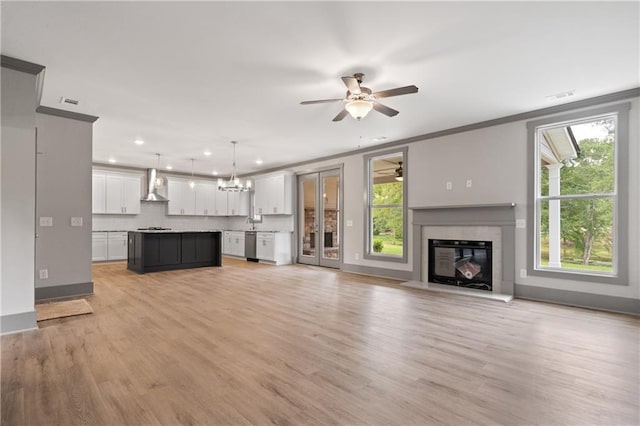 unfurnished living room with ornamental molding, a high end fireplace, ceiling fan with notable chandelier, and light hardwood / wood-style flooring