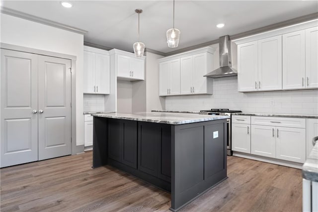 kitchen featuring decorative light fixtures, white cabinets, wall chimney range hood, light stone countertops, and stainless steel range with gas stovetop