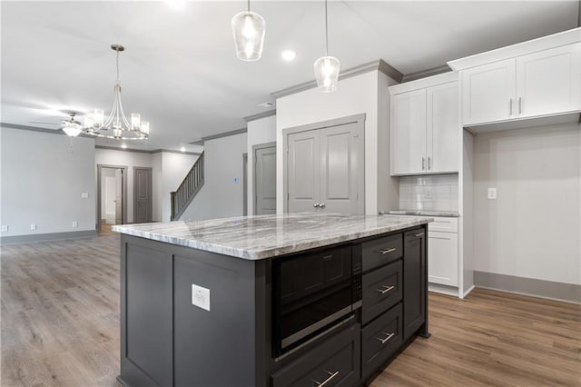 kitchen with pendant lighting, white cabinetry, decorative backsplash, a center island, and light stone counters