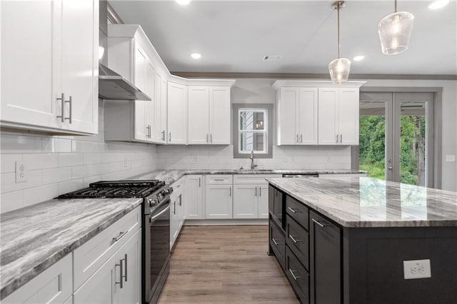 kitchen featuring white cabinetry, a center island, light stone counters, decorative light fixtures, and stainless steel range with gas cooktop