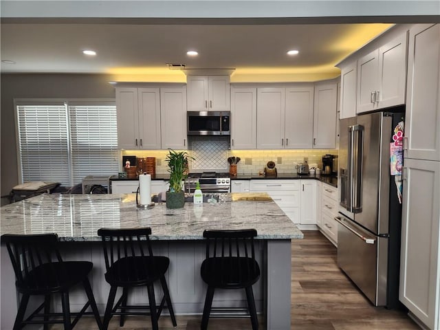 kitchen featuring high quality appliances, a large island with sink, a kitchen bar, and dark stone counters