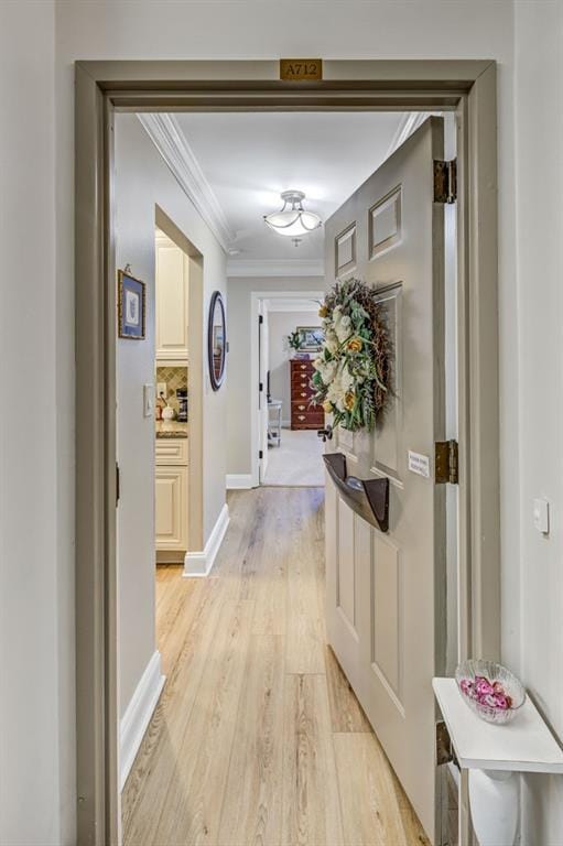 corridor with ornamental molding, light wood-style floors, and baseboards