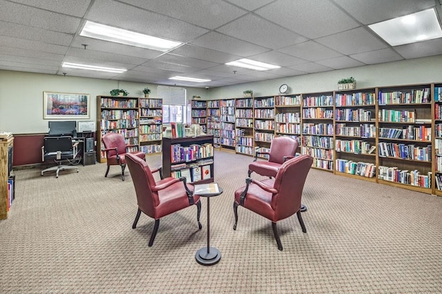 sitting room with light carpet, bookshelves, and a paneled ceiling