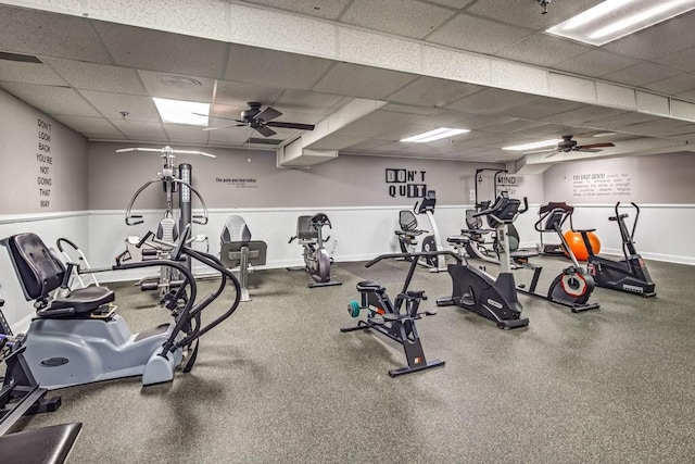 exercise room with a drop ceiling, a ceiling fan, and baseboards