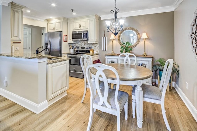 kitchen with light stone counters, stainless steel appliances, a sink, hanging light fixtures, and light wood finished floors