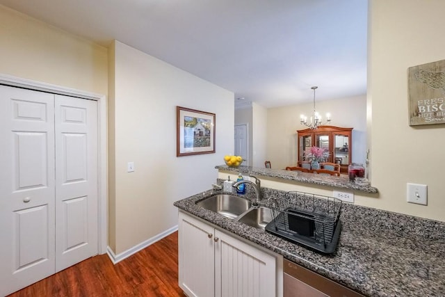 kitchen featuring a notable chandelier, a sink, dark wood finished floors, dark stone countertops, and white cabinetry