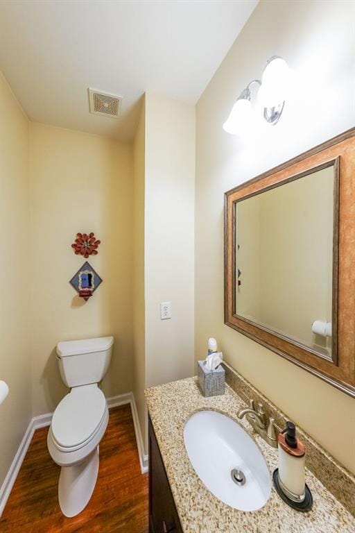 bathroom with vanity, toilet, baseboards, wood finished floors, and visible vents