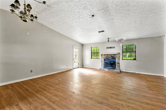 unfurnished living room featuring a chandelier, wood finished floors, a textured ceiling, a stone fireplace, and baseboards
