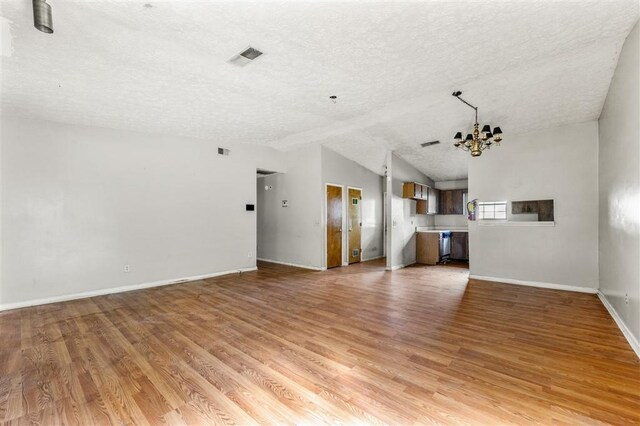 unfurnished living room featuring a textured ceiling, a chandelier, vaulted ceiling, light wood-style flooring, and baseboards