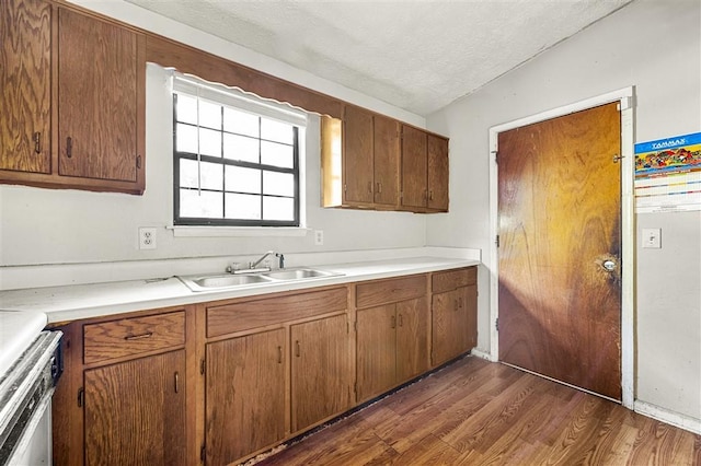 kitchen featuring dark wood-style flooring, light countertops, a textured ceiling, a sink, and brown cabinetry