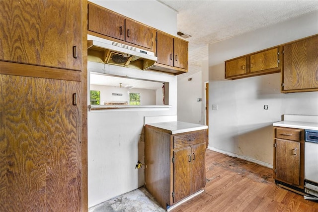 kitchen with brown cabinets, under cabinet range hood, light countertops, and light wood-type flooring