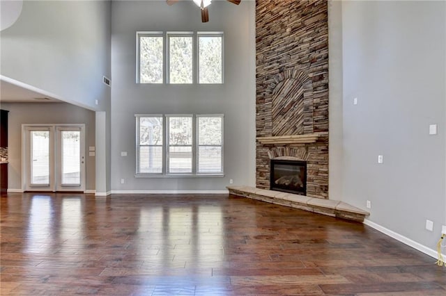 unfurnished living room featuring a high ceiling, a wealth of natural light, dark hardwood / wood-style floors, and a stone fireplace