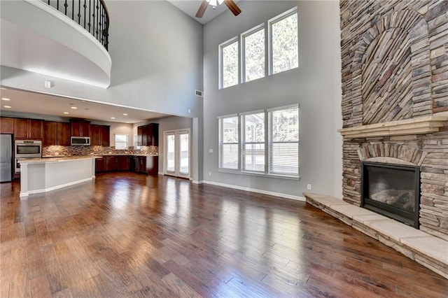 unfurnished living room with ceiling fan, dark hardwood / wood-style floors, a stone fireplace, and a towering ceiling