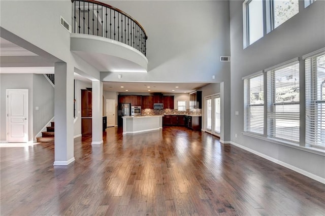 unfurnished living room featuring decorative columns, a high ceiling, and dark hardwood / wood-style flooring