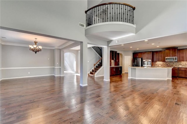 unfurnished living room featuring a high ceiling, dark hardwood / wood-style flooring, ornamental molding, and a chandelier