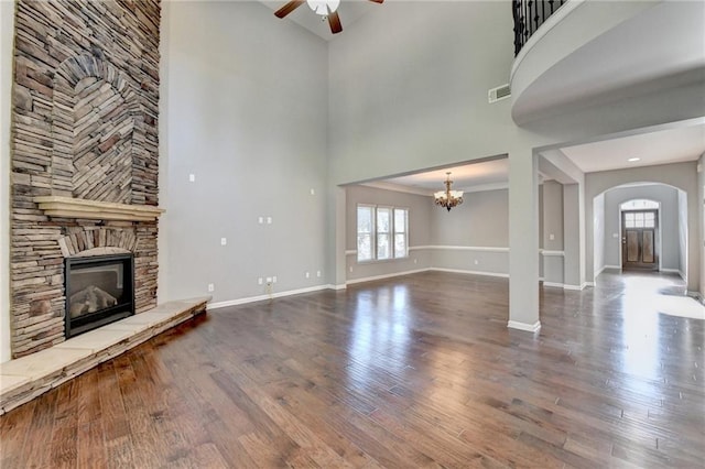 unfurnished living room featuring ceiling fan with notable chandelier, a towering ceiling, hardwood / wood-style flooring, and a stone fireplace