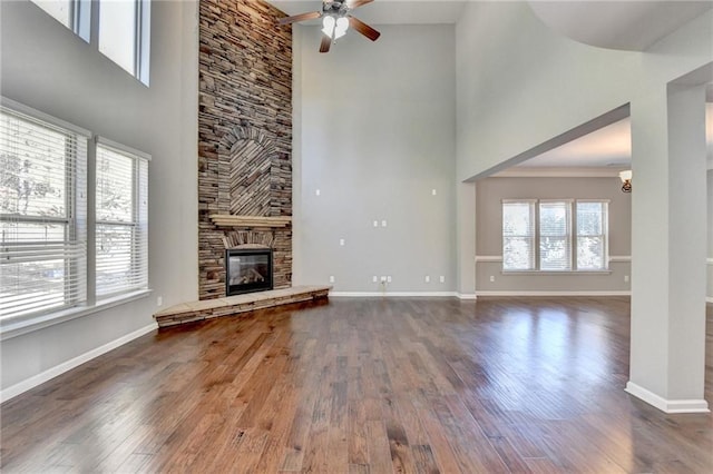 unfurnished living room with ceiling fan, dark wood-type flooring, a towering ceiling, and a fireplace