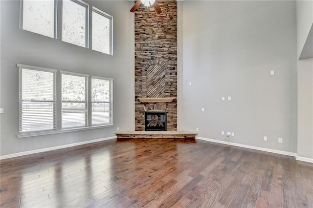 unfurnished living room featuring a towering ceiling, a stone fireplace, ceiling fan, and dark hardwood / wood-style floors