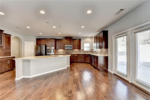 kitchen with a center island, stainless steel appliances, decorative backsplash, light wood-type flooring, and light stone counters