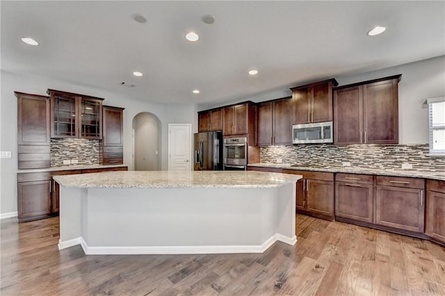 kitchen with a kitchen island, light stone counters, light hardwood / wood-style flooring, and fridge with ice dispenser