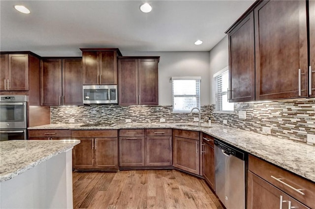 kitchen featuring sink, light wood-type flooring, light stone counters, decorative backsplash, and stainless steel appliances