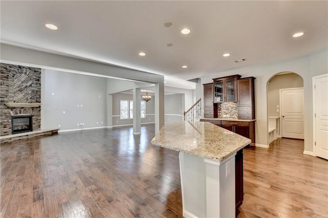 kitchen featuring hardwood / wood-style flooring, tasteful backsplash, light stone counters, a fireplace, and a center island