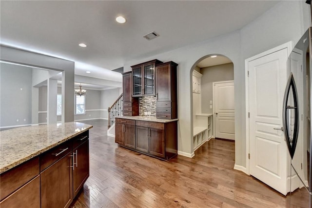 kitchen featuring light wood-type flooring, decorative backsplash, light stone counters, black fridge, and dark brown cabinetry