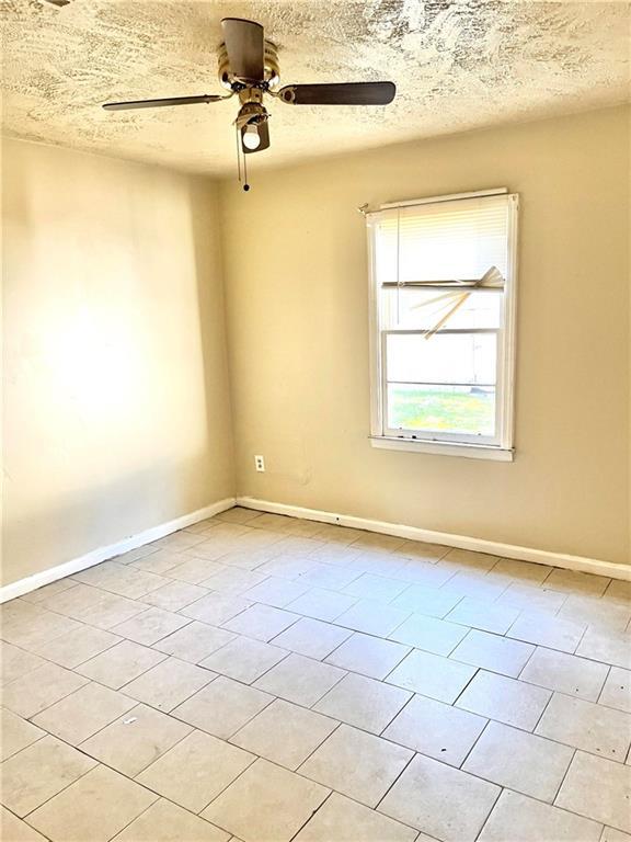 empty room with ceiling fan, a textured ceiling, and light tile patterned floors