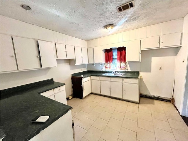 kitchen featuring white cabinetry, sink, light tile patterned floors, and a textured ceiling