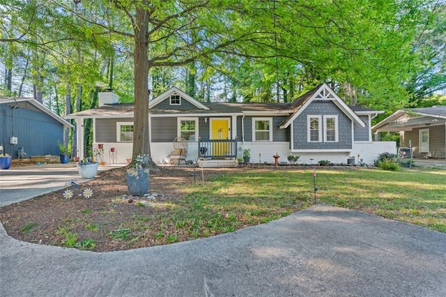 view of front of house featuring a chimney, covered porch, and a front lawn