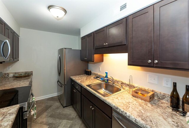 kitchen featuring stainless steel appliances, dark brown cabinets, sink, and light stone counters